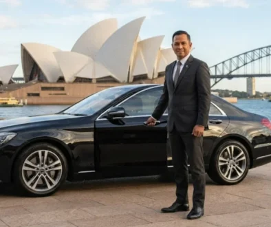 Professional chauffeur standing beside a luxury black Mercedes vehicle in front of the Sydney Opera House.
